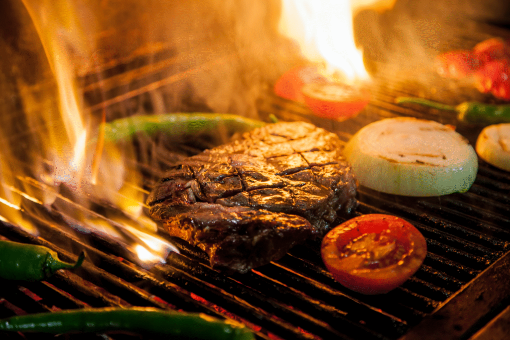 Saftiges Steak mit Tomaten, Zwiebeln und grünen Peperoni über offenen Flammen auf dem Grill