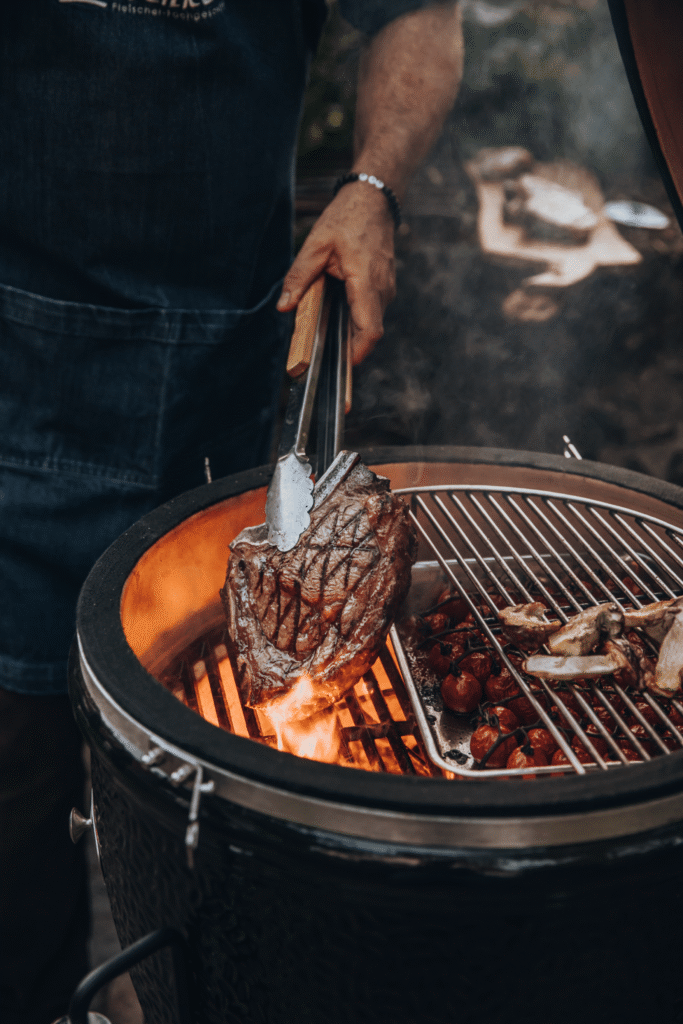 Grillmeister hält ein gegrilltes Steak mit einer Zange über die offene Flamme eines Grills